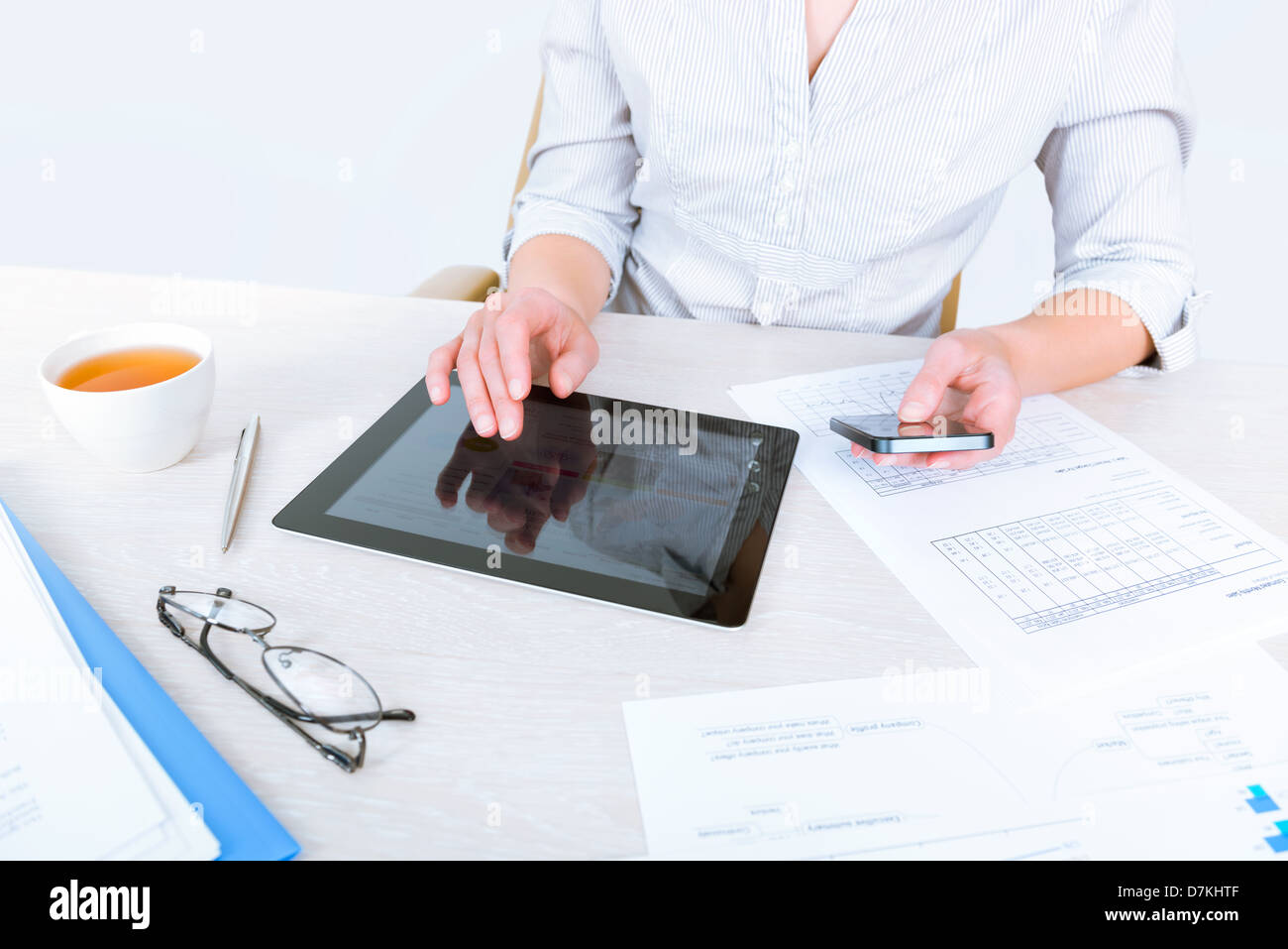 Imprenditrice di successo seduto alla scrivania e contemporaneamente utilizzando i moderni dispositivi per la comunicazione aziendale Foto Stock