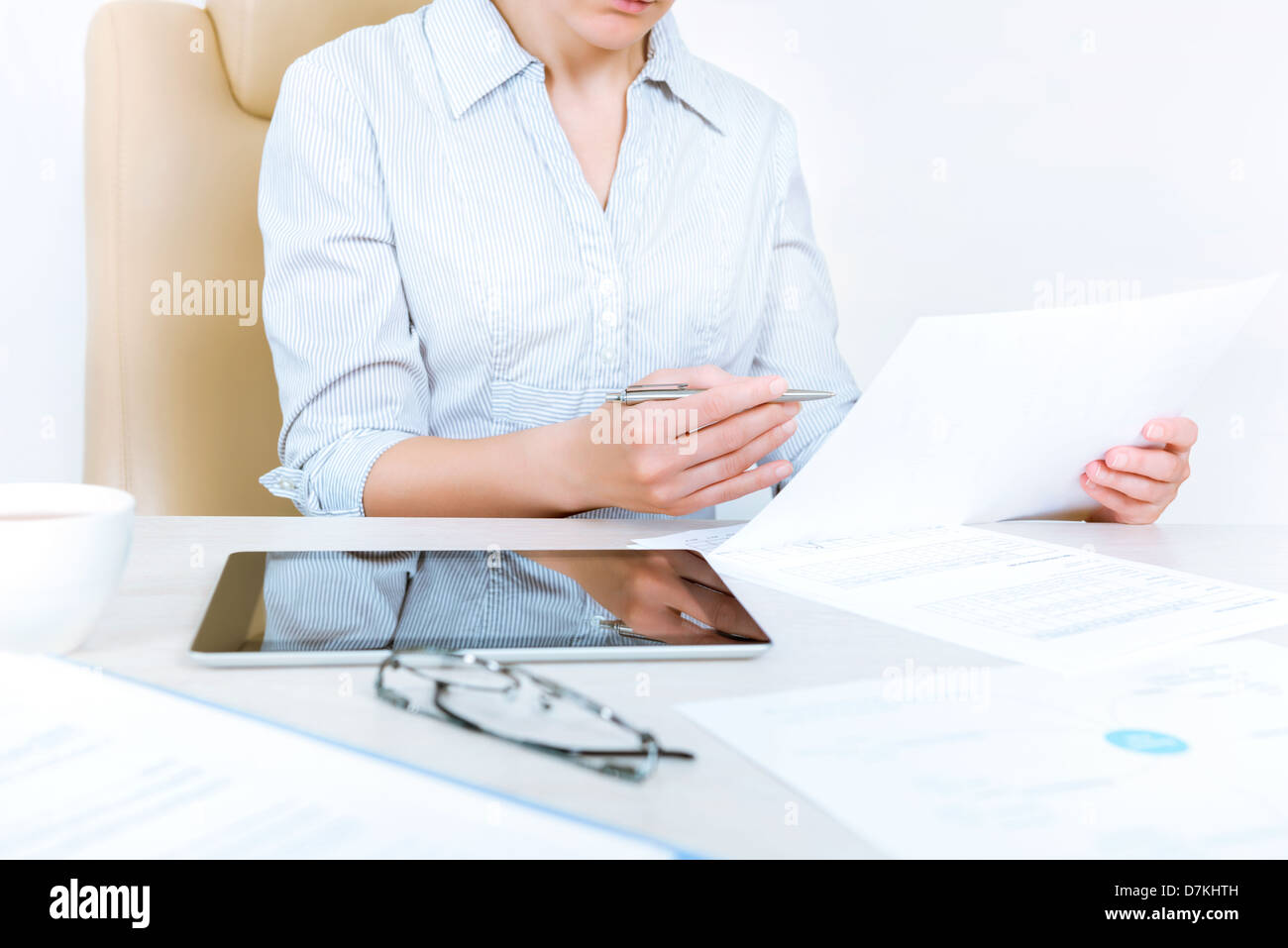 Occupato imprenditrice che indossa in camicia casual seduto alla scrivania e controllare i documenti in ufficio Foto Stock