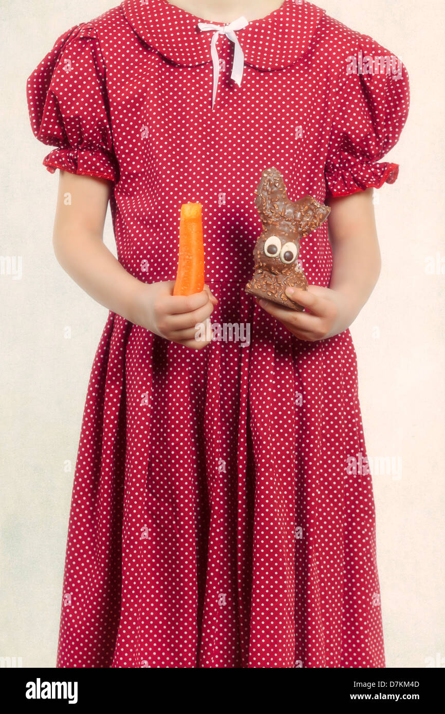 Sana e malsano - una ragazza con una carota e un coniglio di cioccolato Foto Stock