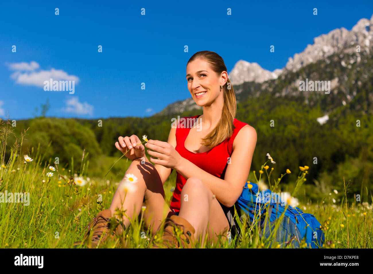 Felice giovane donna seduta con fiore in mano nel prato con vista montagna Foto Stock
