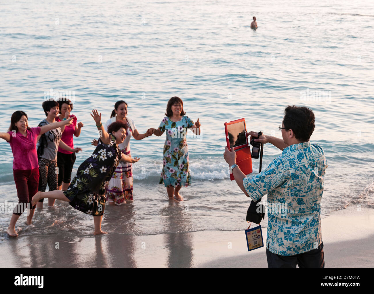 Un Cinese uomo asiatico con un computer tablet prende la foto di un gruppo di turisti cinesi sulla spiaggia di Waikiki, Honolulu, Hawaii. Foto Stock