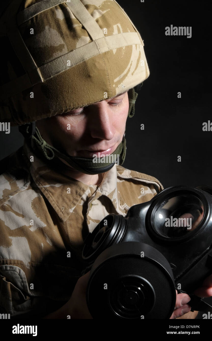 Soldato tenendo un respiratore e indossando militare inglese desert camouflage uniforme, contro uno sfondo nero. Foto Stock