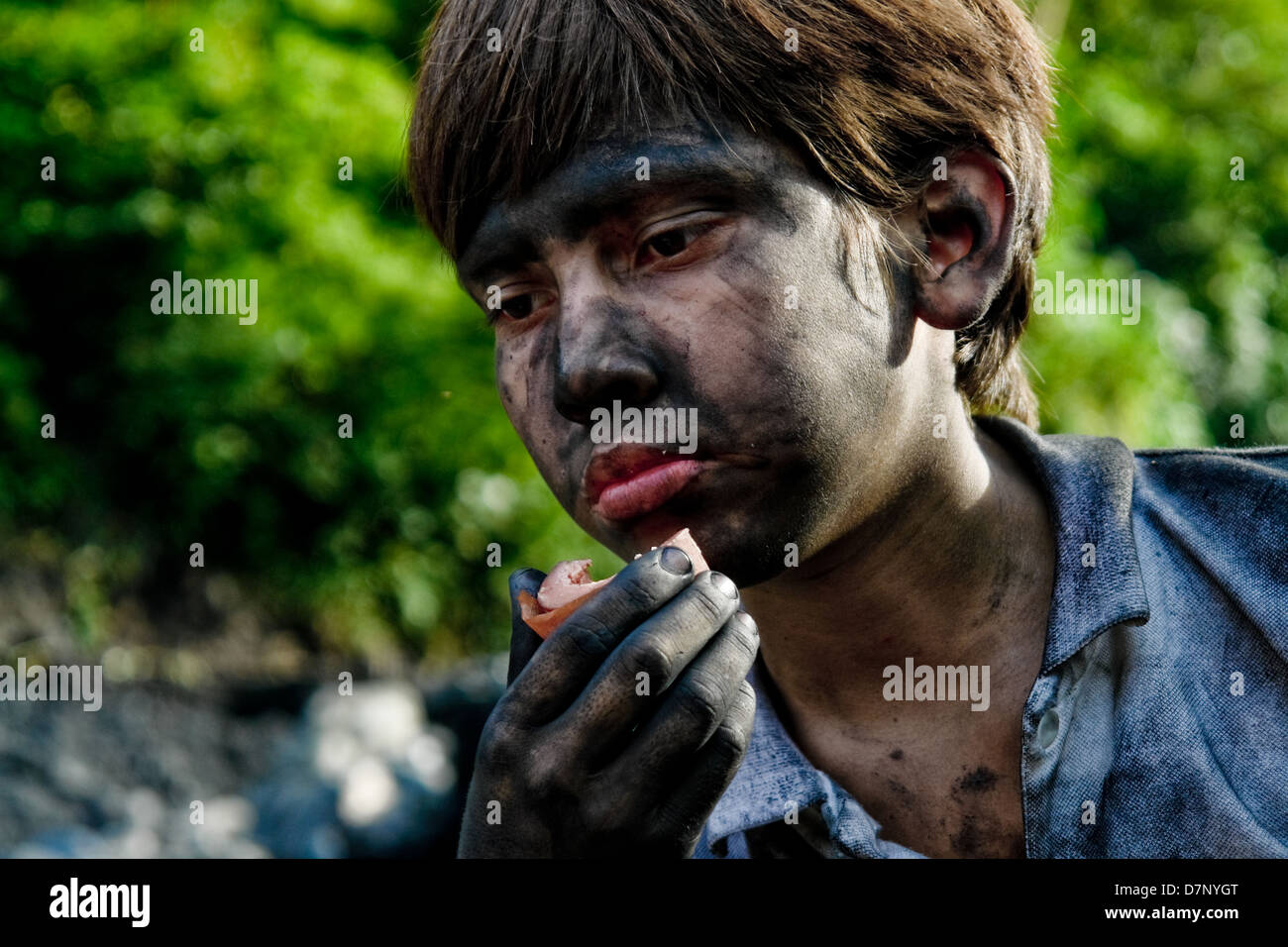 Un giovane ragazzo mangia la salsiccia dopo aver finito il suo turno di lavoro nella miniera di smeraldo di Muzo, Colombia. Foto Stock