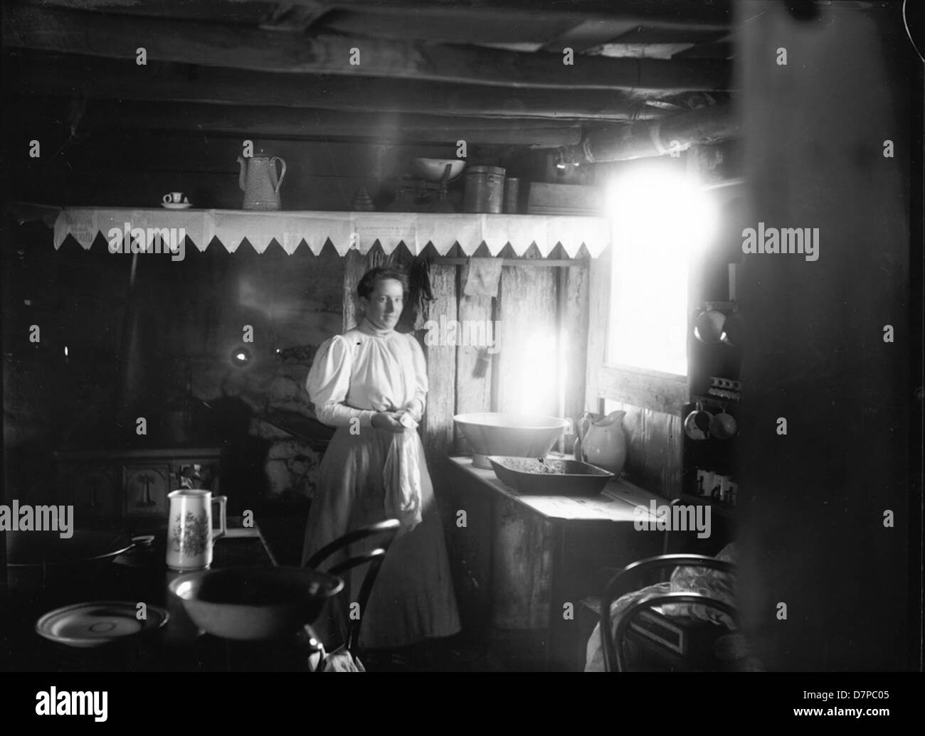 Questa fotografia cattura una donna all'interno di una capanna di coloni, mostrando la vita domestica nella prima Australia coloniale. L'immagine fornisce informazioni sui compiti quotidiani e sulle condizioni di vita dei coloni durante il XIX secolo, mettendo in evidenza gli articoli per la casa e l'abbigliamento. Foto Stock