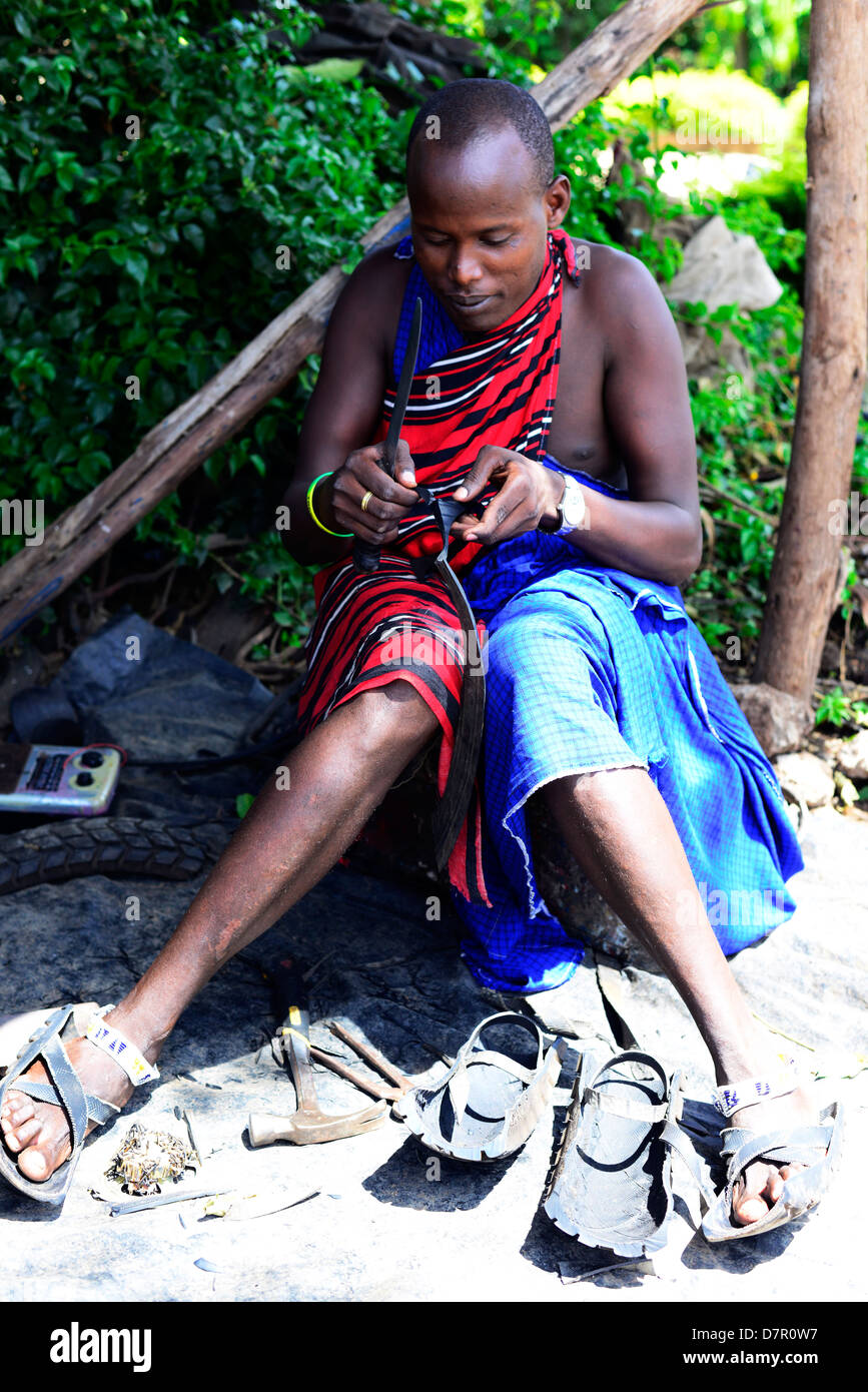 Un calzolaio Masai lavorando su una nuova coppia di Masai sandali fatti di vecchio livello ruote. Foto Stock