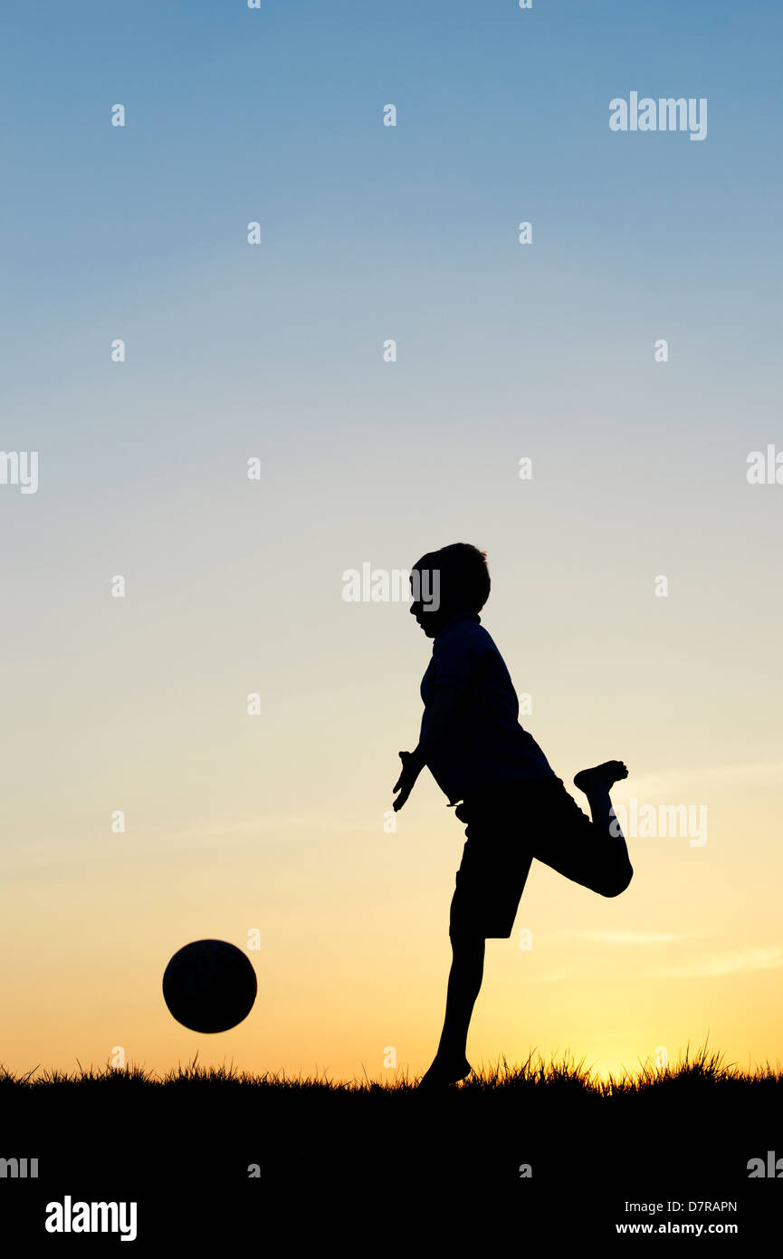 Ragazzo giocando con un calcio al tramonto. Silhouette Foto Stock