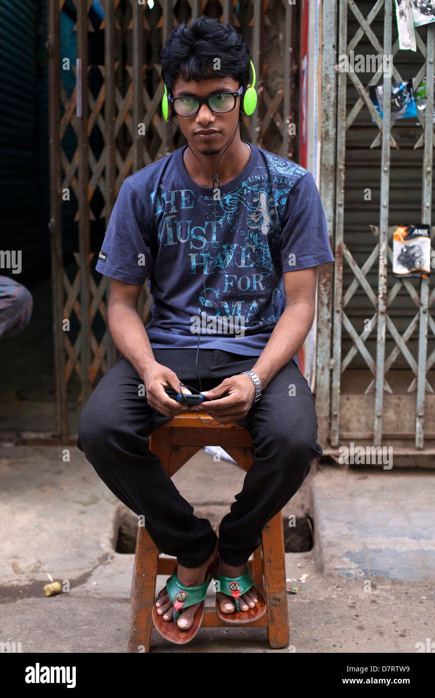 Un vestiti alla moda giovane uomo ascolta la musica sul telefono cellulare con le cuffie, vecchia Dacca in Bangladesh Foto Stock