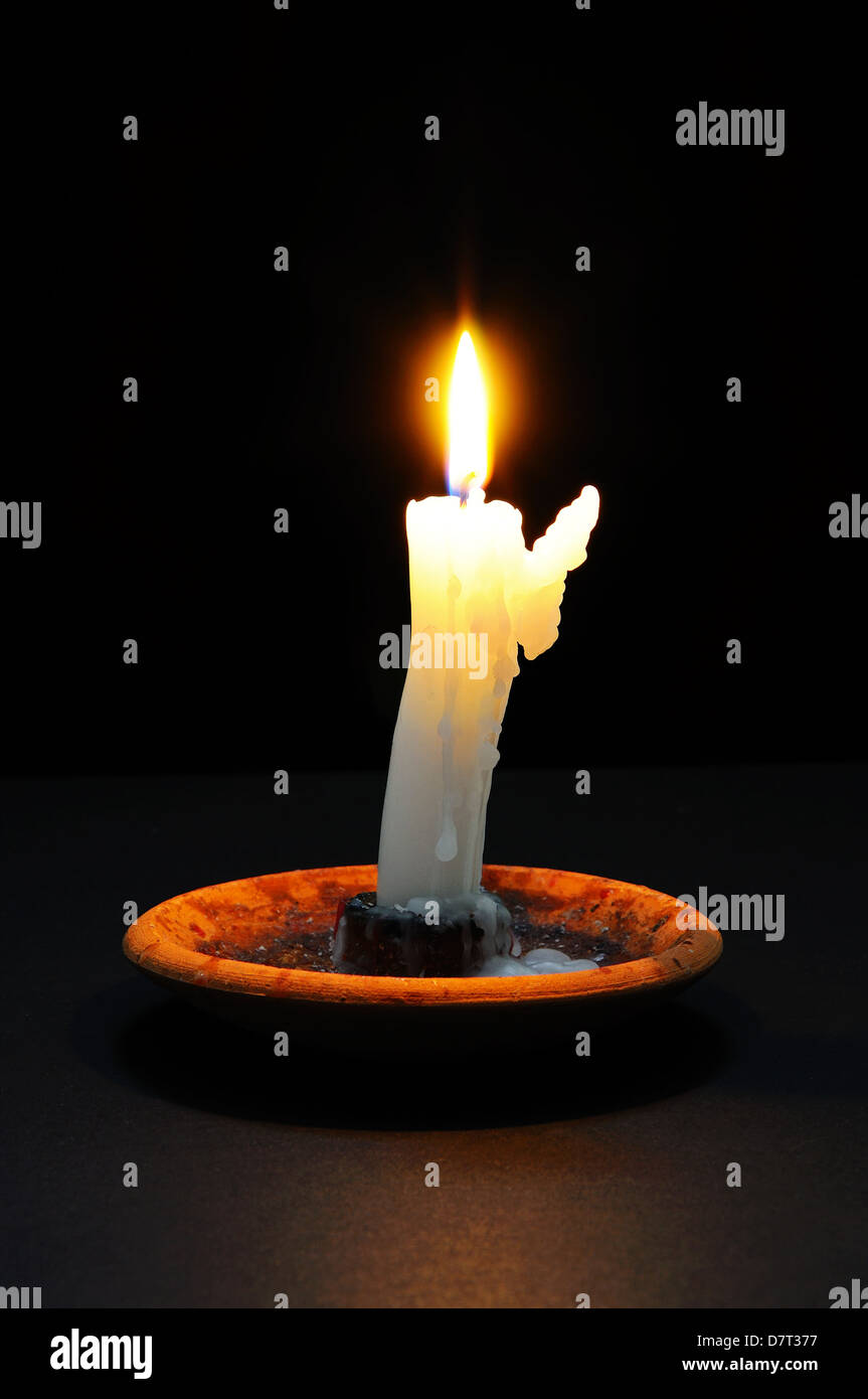 Candela bianca con la cera in esecuzione sul lato in basso a lume di candela contro uno sfondo nero. Foto Stock
