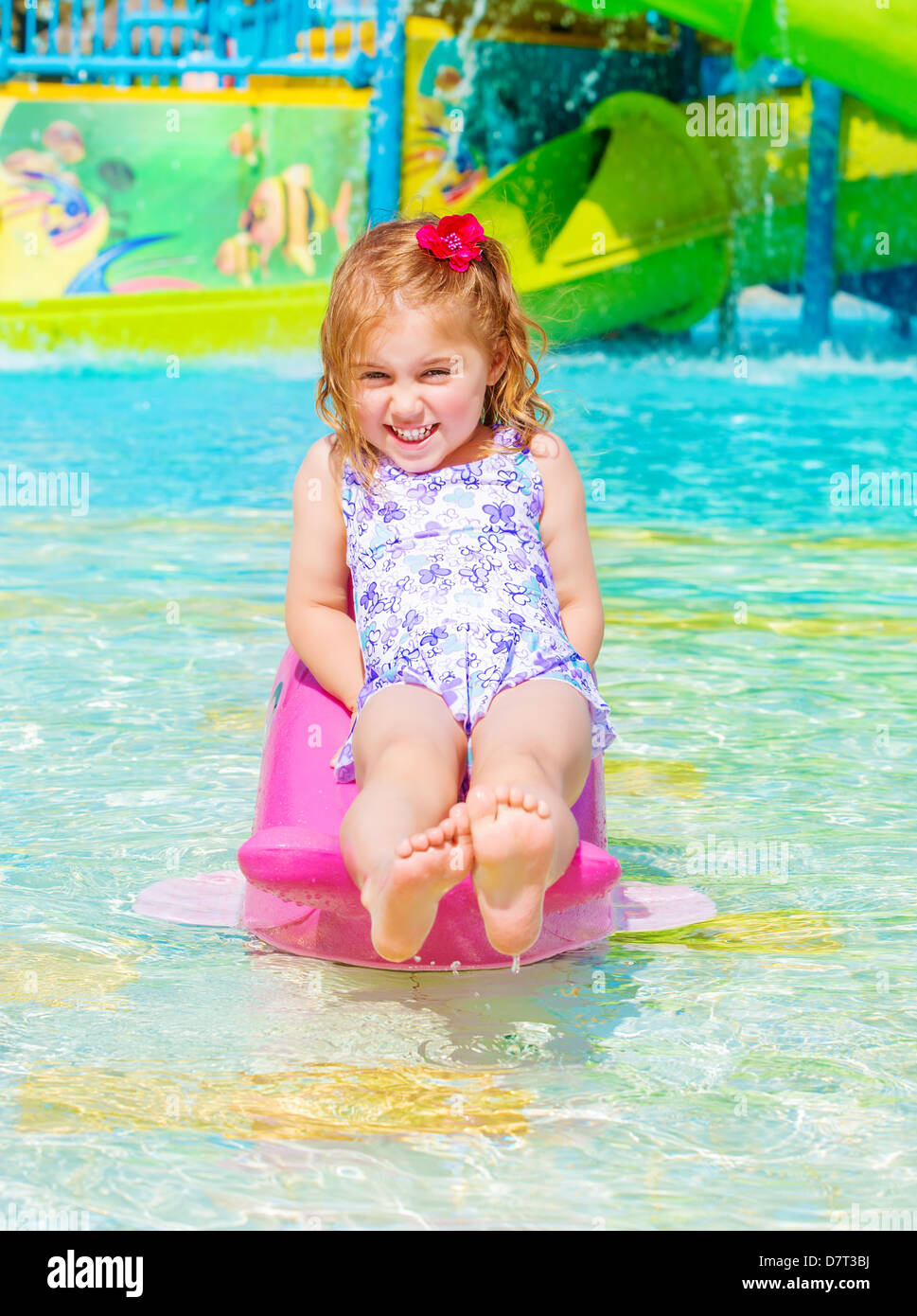 Allegro sorridente bambina godendo di attrazioni acquatiche, giorno caldo e soleggiato, nuoto in piscina, infanzia spensierata, vacanze estive Foto Stock
