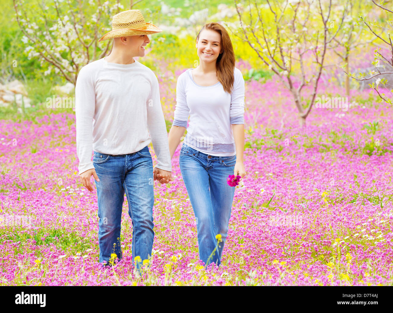 Felice famiglia giovane passeggiate nel parco di primavera, tenendo le mani, rurale di prato, il giardino dei frutti, godendo di vacanza Foto Stock