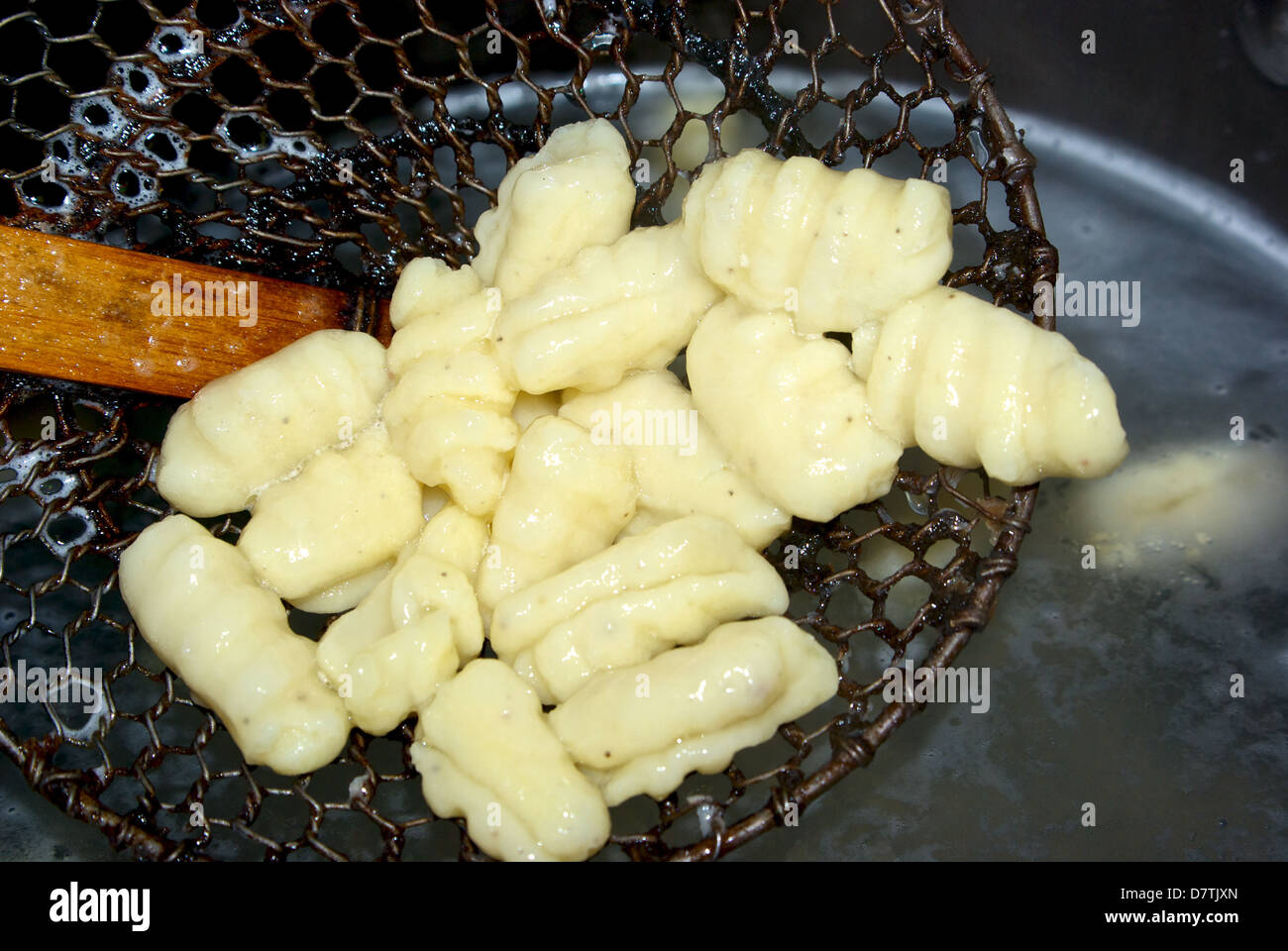 Cucinato increspato e arricciato gnocchi di pasta di patate che viene sollevato dalla pentola di acqua bollente con reticella di metallo Foto Stock