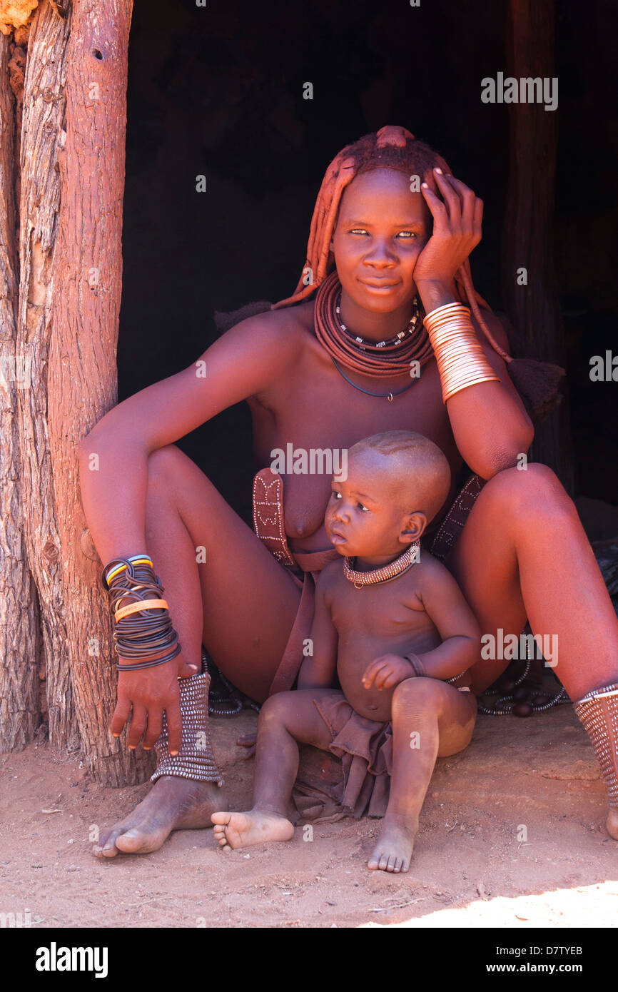 Donna Himba, con baby, indossando abiti e gioielli e con la sua pelle ricoperta in Otjize,, Regione di Kunene, Kaokoland, Namibia Foto Stock