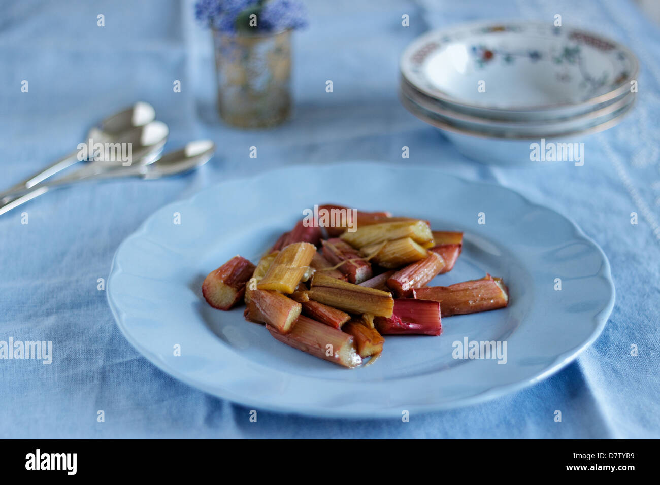 Rabarbaro sulla piastra blu con posate e tazze da dessert. Foto Stock