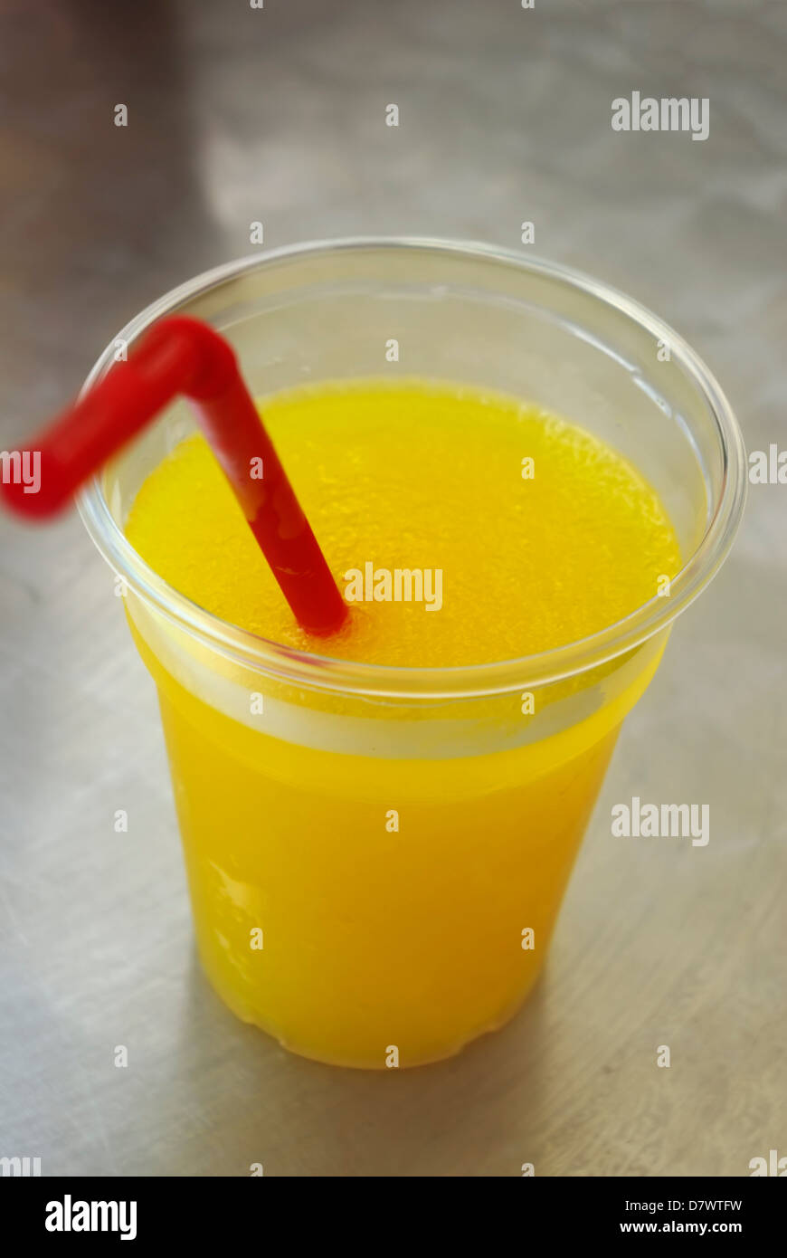 Bicchiere di plastica sul tavolo con ghiaccio giallo bevanda fredda e paglia di rosso. Foto Stock