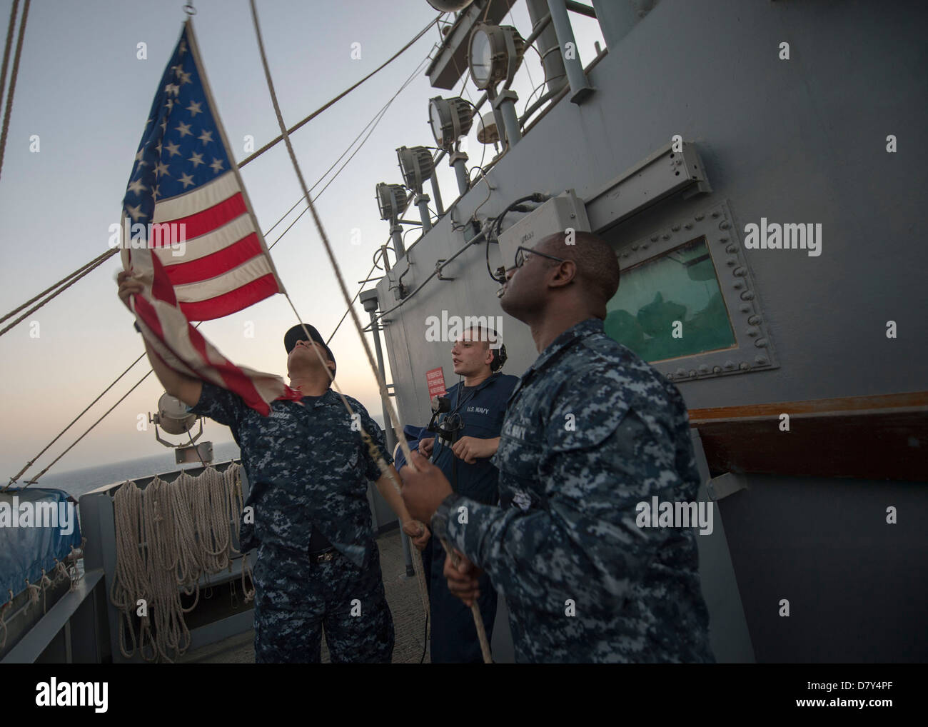 I marinai abbassare il national ensign. Foto Stock
