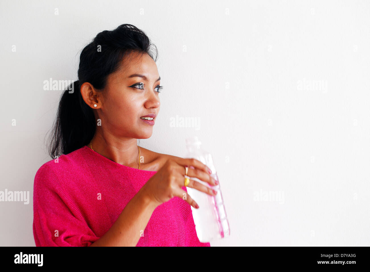 Giovane donna in una rosa top acqua potabile e in piedi contro un muro bianco Foto Stock