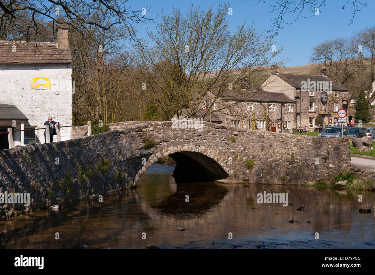L'uomo si innalza dalla storica unica pietra-span bridge over Malham Beck nel centro di scenic Dales villaggio sulla giornata di sole - Malham, North Yorkshire, Inghilterra, Regno Unito Foto Stock