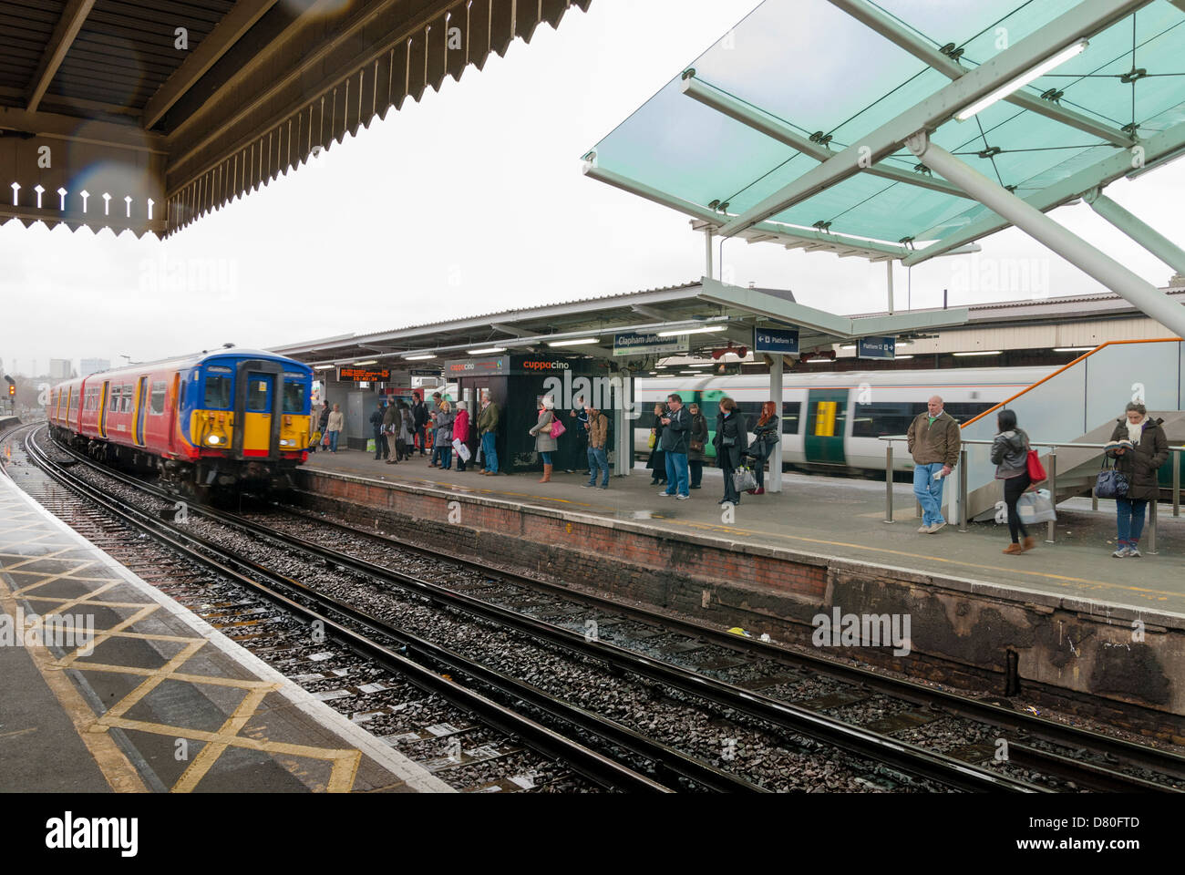 I passeggeri in attesa del treno in arrivo sulla piattaforma a Clapham Junction station Foto Stock