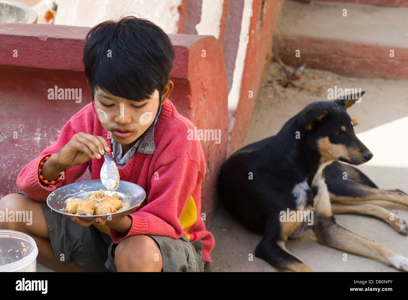 Un giovane ragazzo con il suo cane mangia il pranzo in Mingun, Myanmar 2 Foto Stock