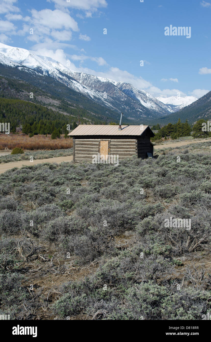 Un vecchio abbandonato log cabin si trova con una vista incredibile della innevate Montagne Rocciose del Colorado. Foto Stock