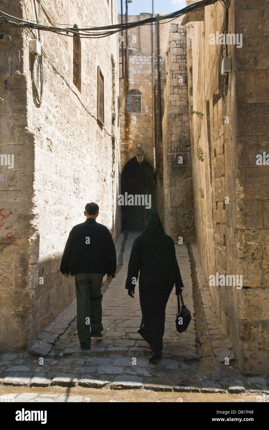 Aleppo Siria. Un uomo e una donna che cammina verso il basso una stretta vecchia strada di ciottoli nel centro della città vecchia, un sito Patrimonio Mondiale dell'UNESCO. Foto Stock