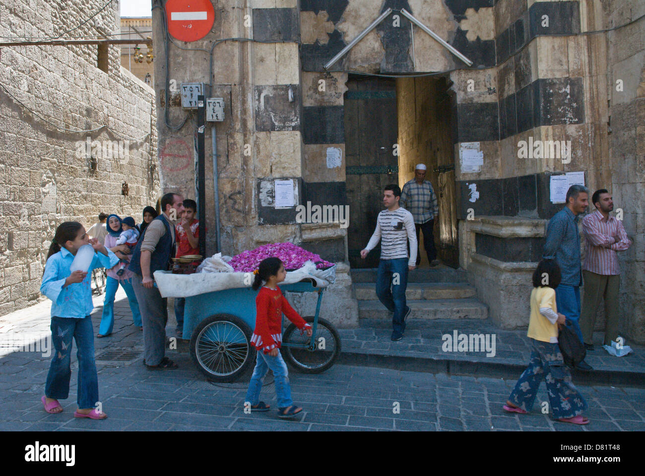 Aleppo, Siria. Persone, compreso un petalo di rosa venditore, in una strada fuori l'ingresso di una vecchia moschea nel centro della città vecchia Foto Stock