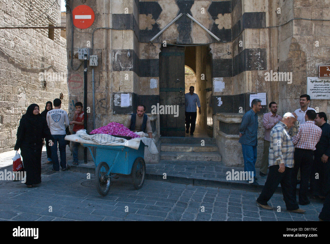 Aleppo, Siria. Le persone al di fuori dell'ingresso di una vecchia moschea nel centro della città vecchia, con un uomo vendita di petali di rosa da un carrello Foto Stock