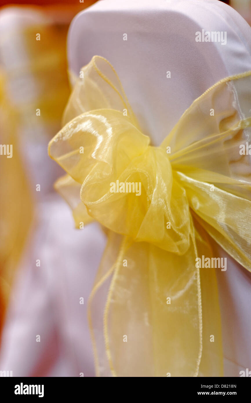 Nastro giallo legato in un arco sulla sedia bianca coperchio Foto Stock