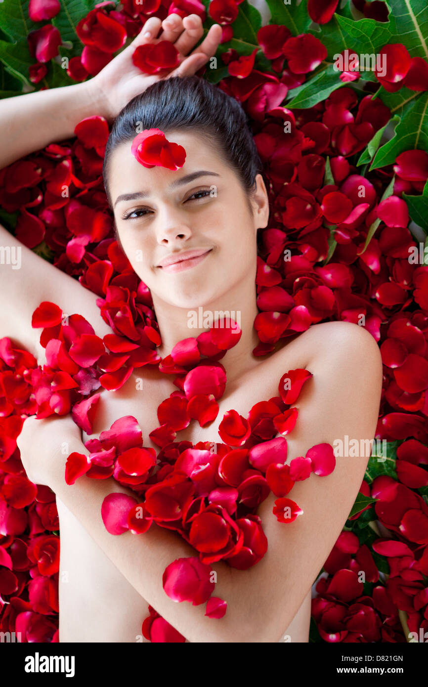 Giovane donna sdraiata sulla schiena contro i petali di rose. Foto Stock