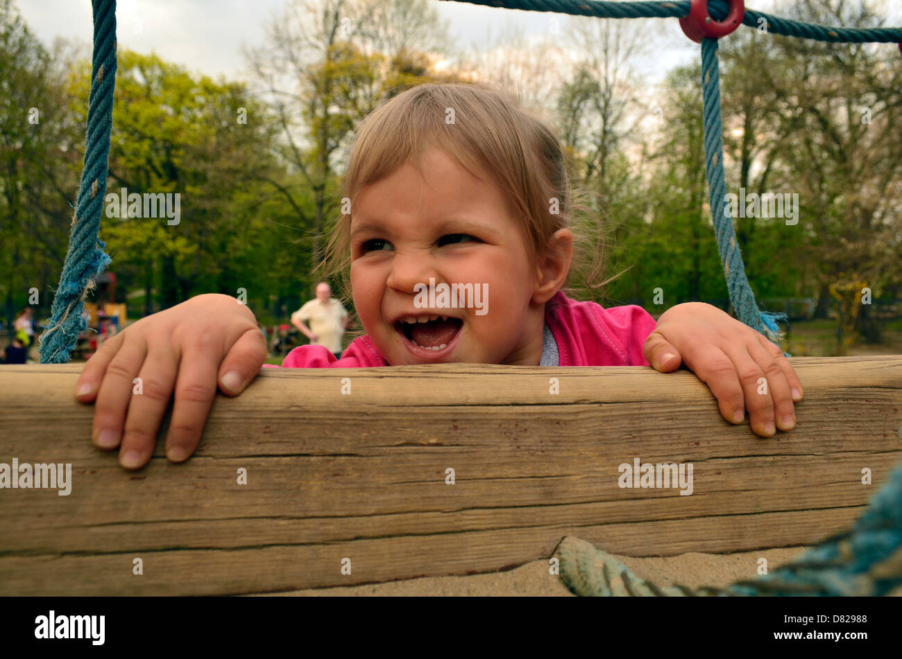 2 anno vecchia ragazza arrampicata sulla palestra della giungla presso il parco giochi sorridente Foto Stock