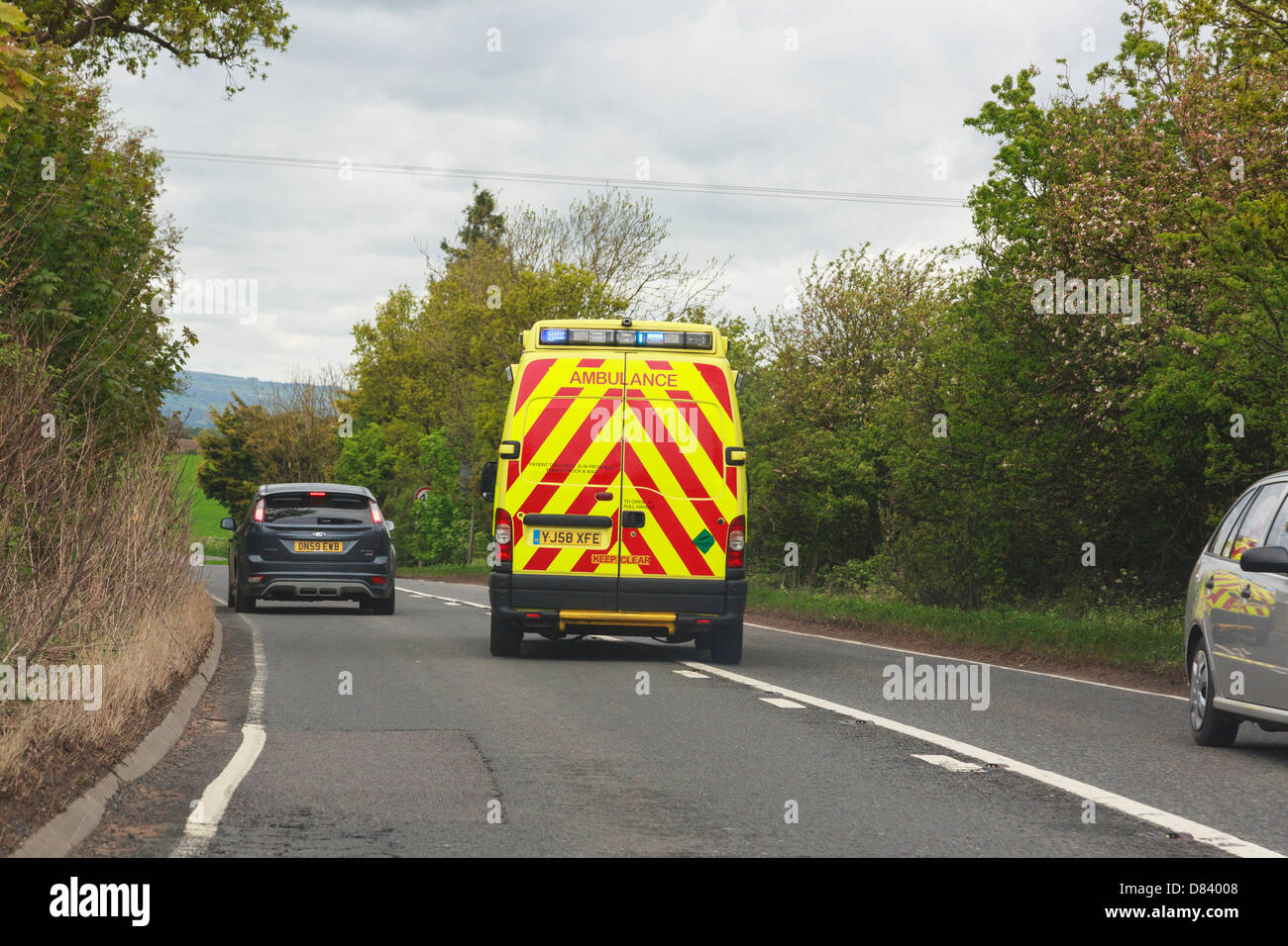 Vista attraverso un parabrezza di un'ambulanza con luci blu lampeggia in fretta in caso di emergenza il sorpasso di un auto lungo la strada principale. Shropshire England Regno Unito Foto Stock