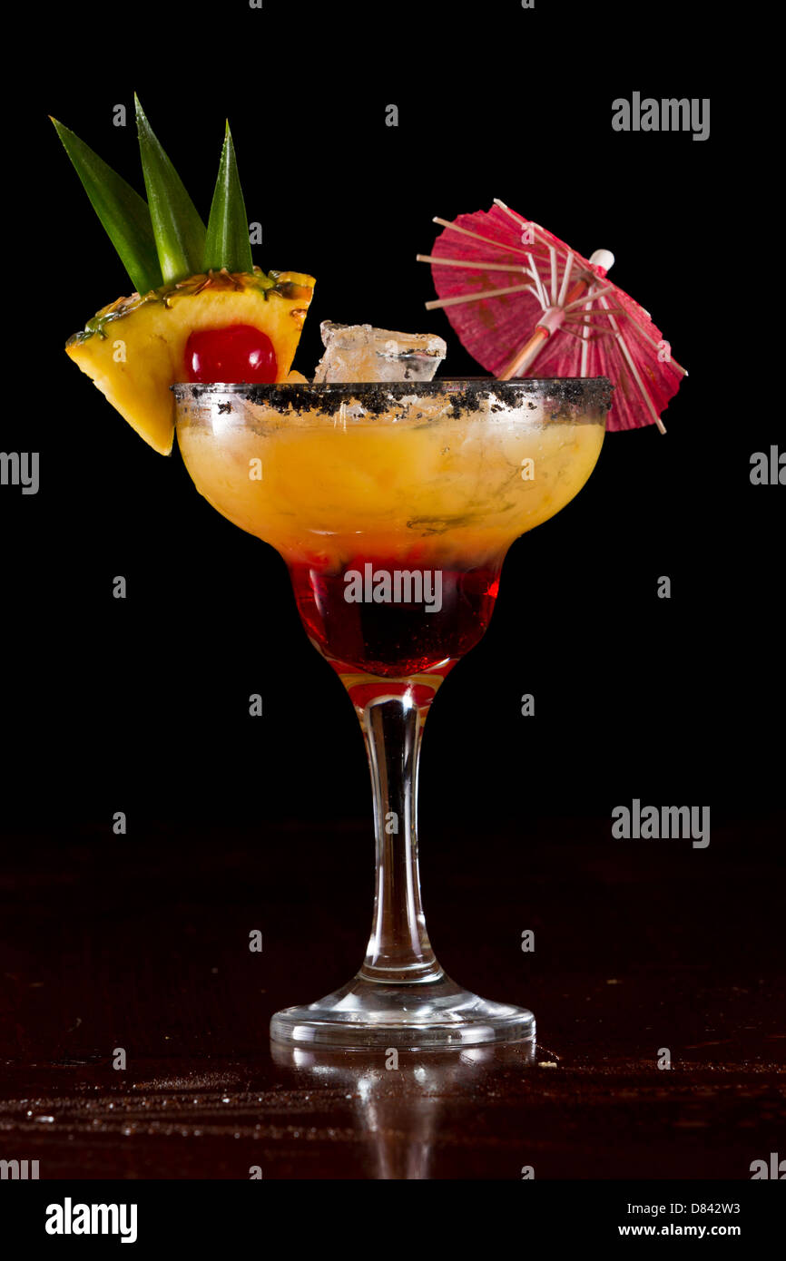 Bella tropical cocktail servito in un bicchiere Margarita con sale nero sul cerchio e una fetta di ananas con una ciliegia in esso Foto Stock
