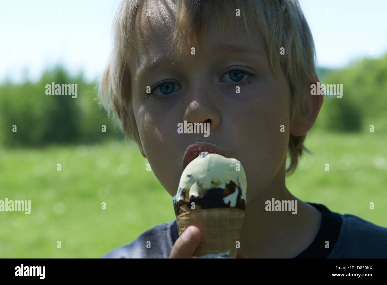 Bambino biondo 6-8 anno vecchio ragazzo trattiene e mangiare il gelato estate Foto Stock