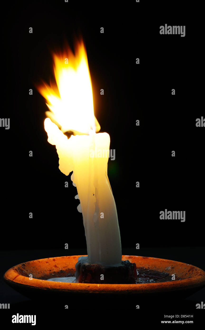 Candela bianca con la cera in esecuzione sul lato in basso a lume di candela contro uno sfondo nero. Foto Stock