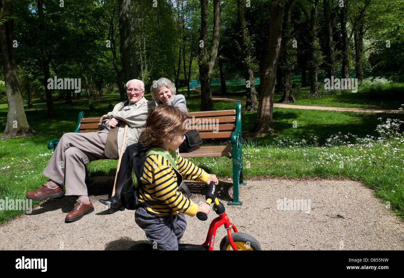 Coppie di anziani nonni seduti sulla panchina che si divertono a guardare un bambino in bicicletta a Bute Park Cardiff Galles UK KATHY DEWITT Foto Stock