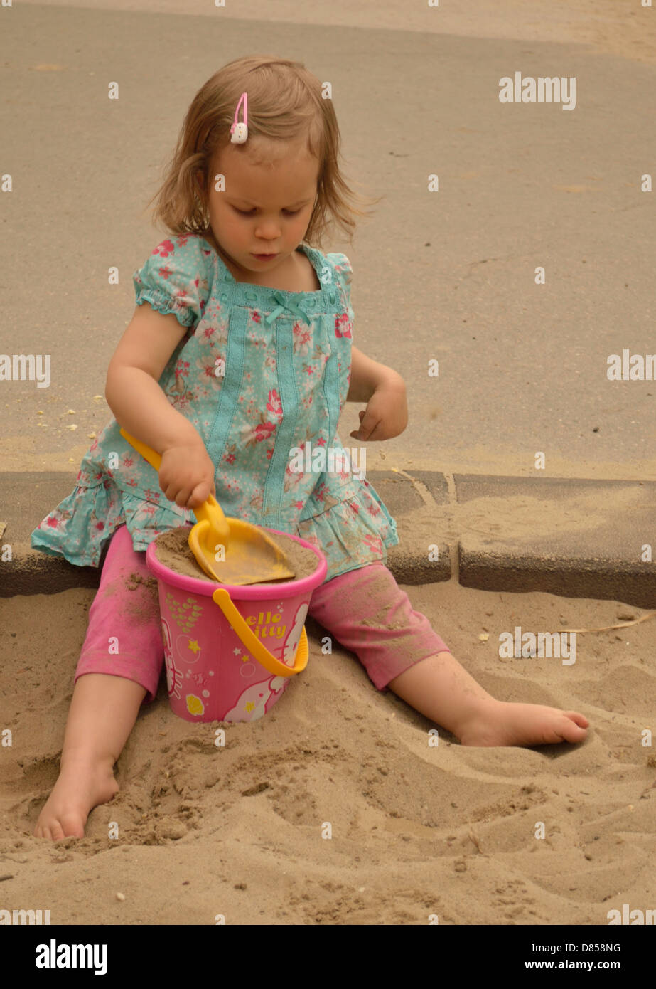 Bambina giocando in sabbia al parco giochi secchio di riempimento con sabbia Foto Stock