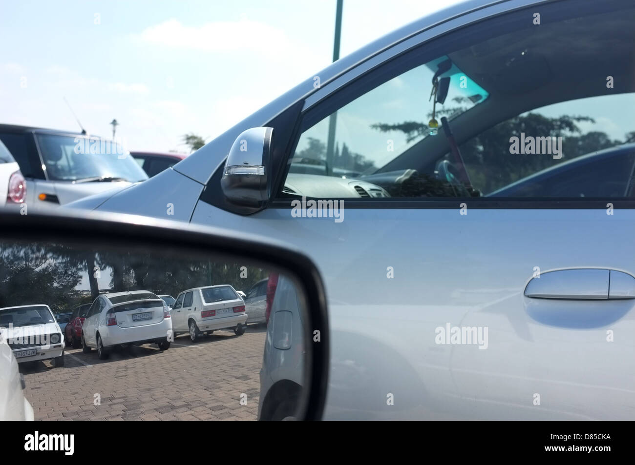 Un parcheggio pieno di auto visibile in dello specchietto retrovisore esterno e attraverso la finestra. Foto Stock