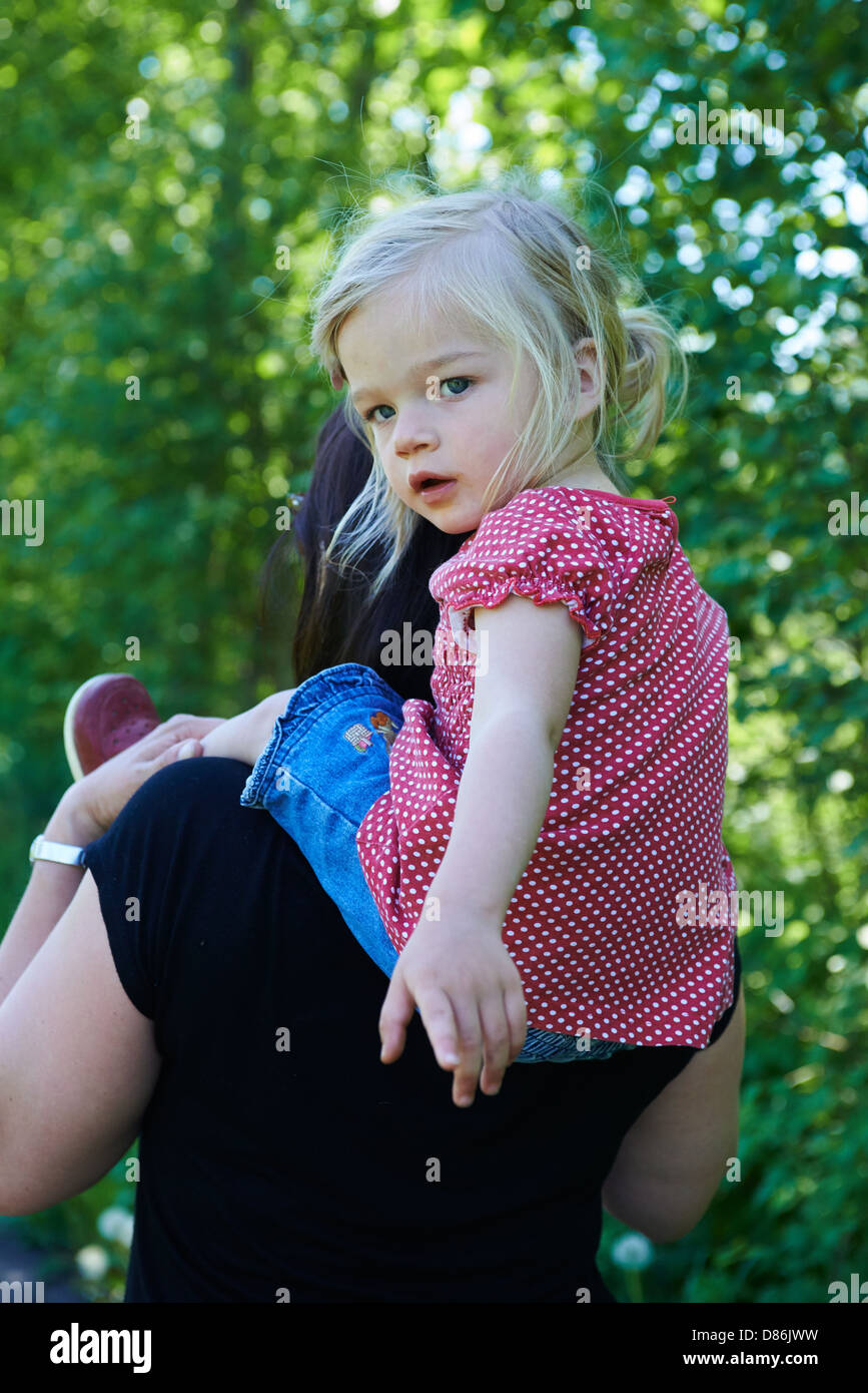 Una ragazza sorridente - figlia ottenendo un piggy back da sua madre nel parco Foto Stock