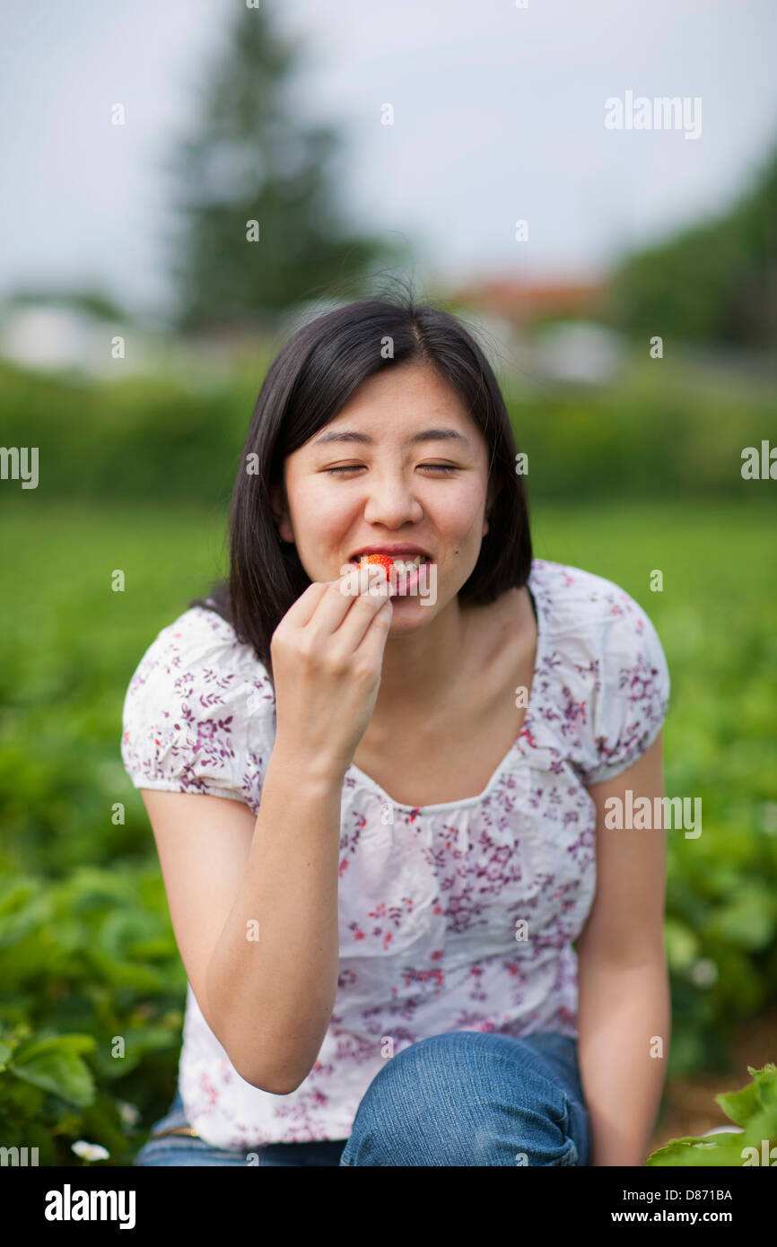 In Germania, in Baviera, giovane donna giapponese mangiare fragole fresche in campo di fragole Foto Stock