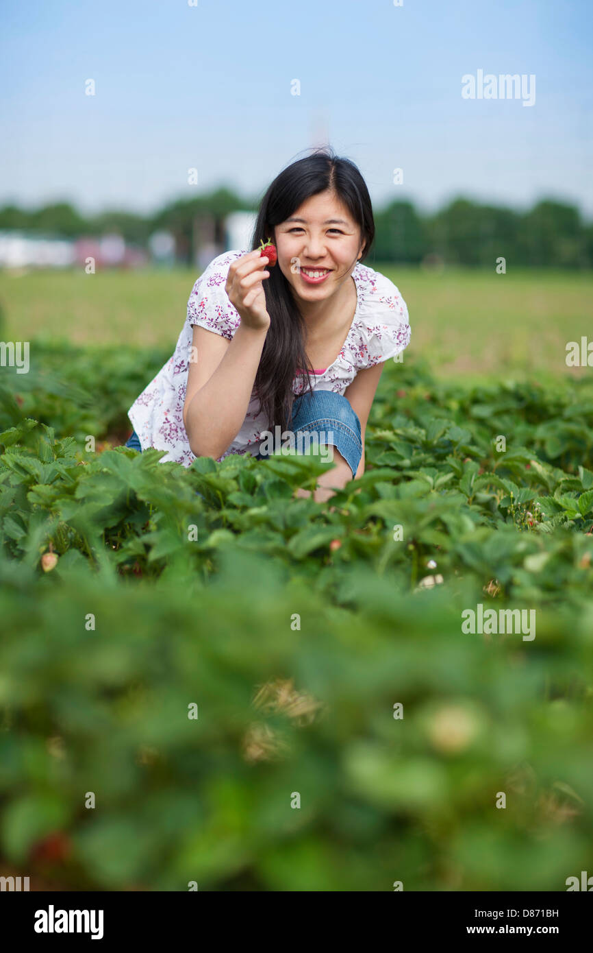 In Germania, in Baviera, giovane donna giapponese che mostra fragola nel campo Foto Stock