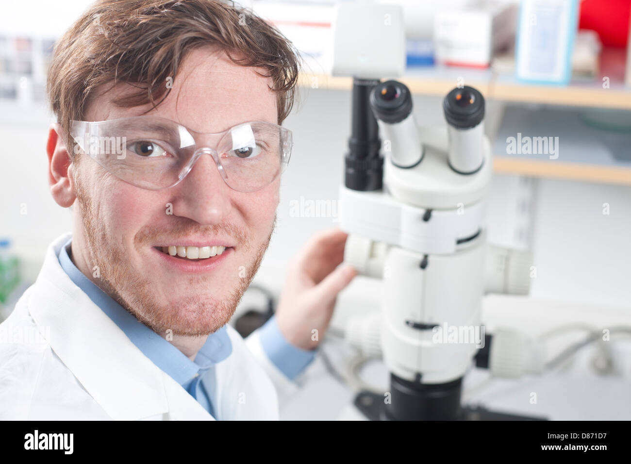 Germania, Ritratto di giovane scienziato con microscopio in laboratorio, sorridente Foto Stock