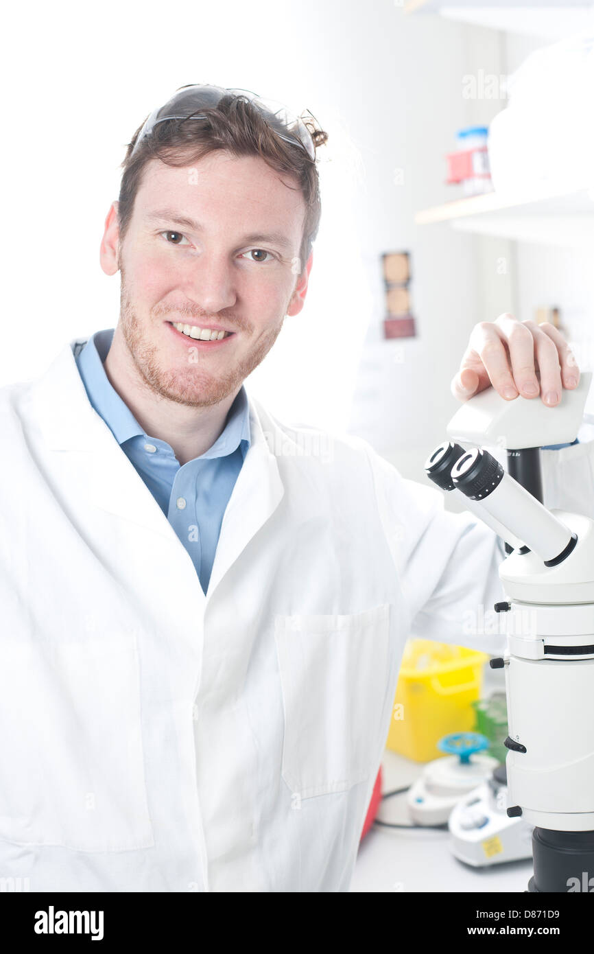 Germania, Ritratto di giovane scienziato con microscopio in laboratorio, sorridente Foto Stock