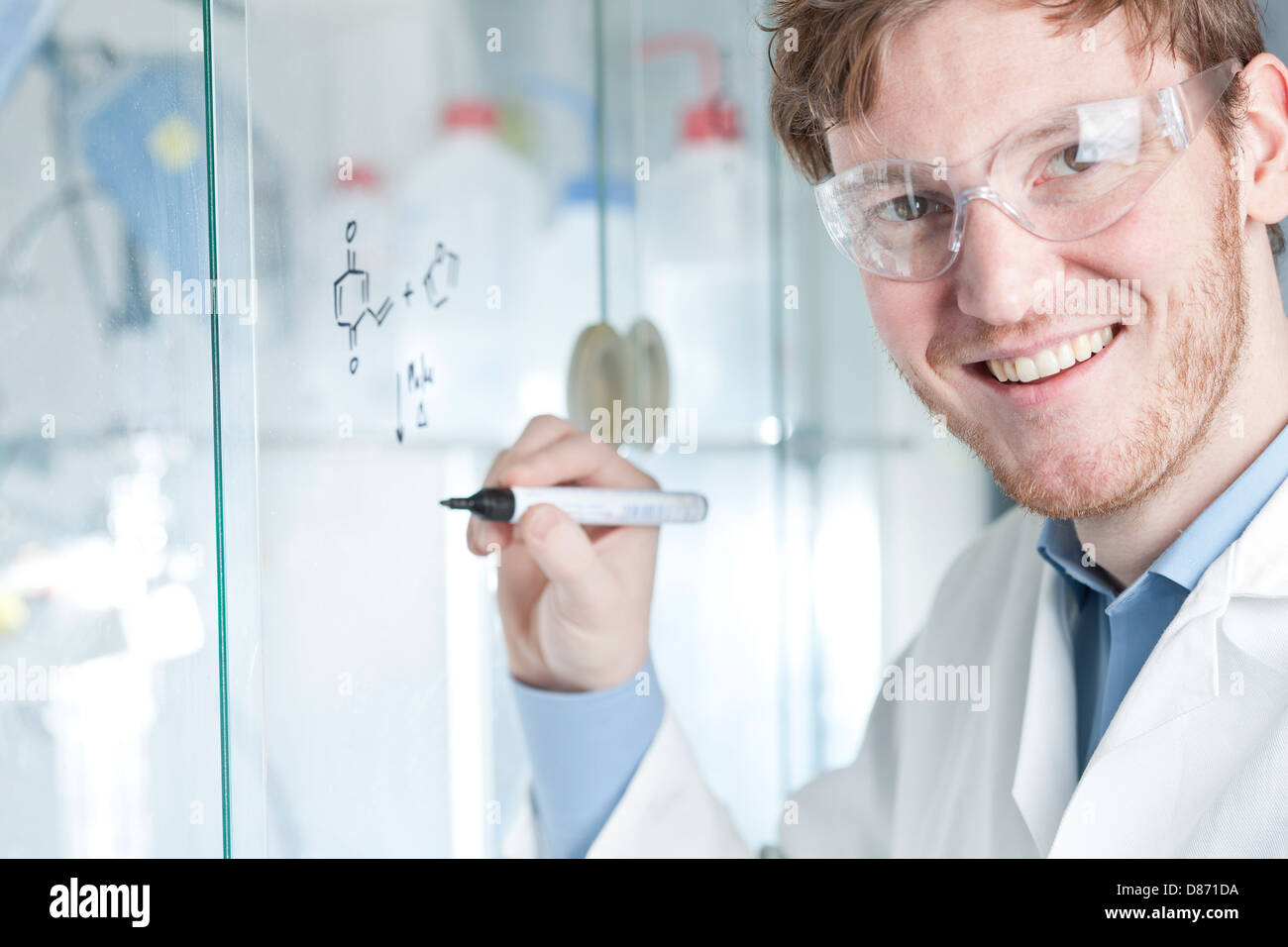 Germania, Ritratto di giovane scienziato scrittura equazione chimica su vetro, sorridente Foto Stock