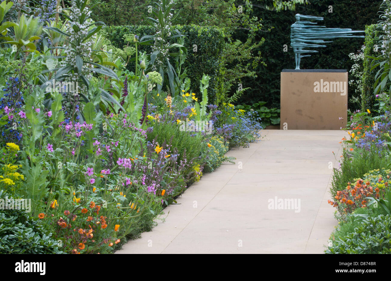 Un piccolo e moderno percorso di giardini all'inglese con bordi di fiori erbacei che fioriscono in estate scultura contemporanea su un plinth UK Foto Stock