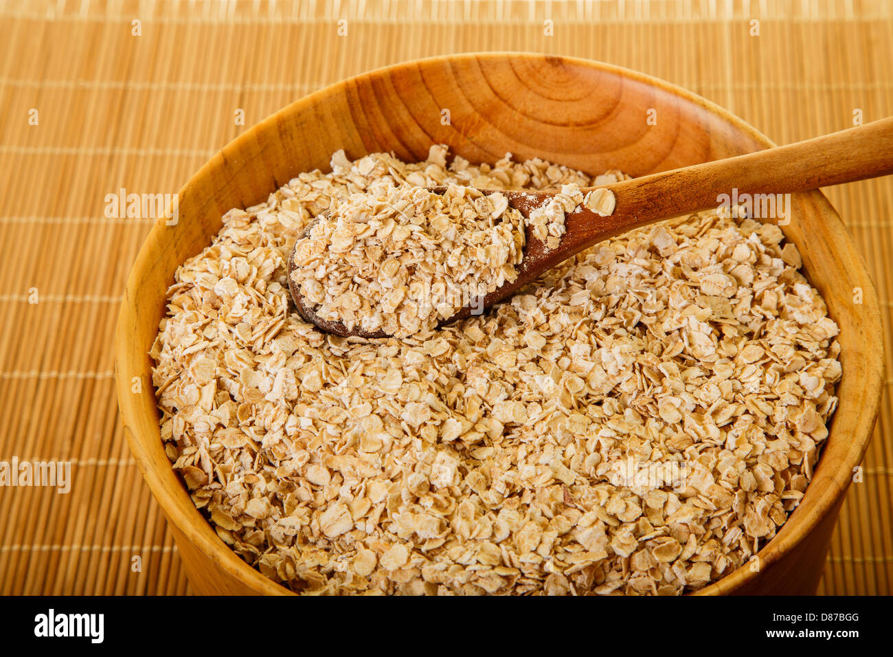 Avena fresca in una ciotola di legno con un cucchiaio di legno Foto Stock