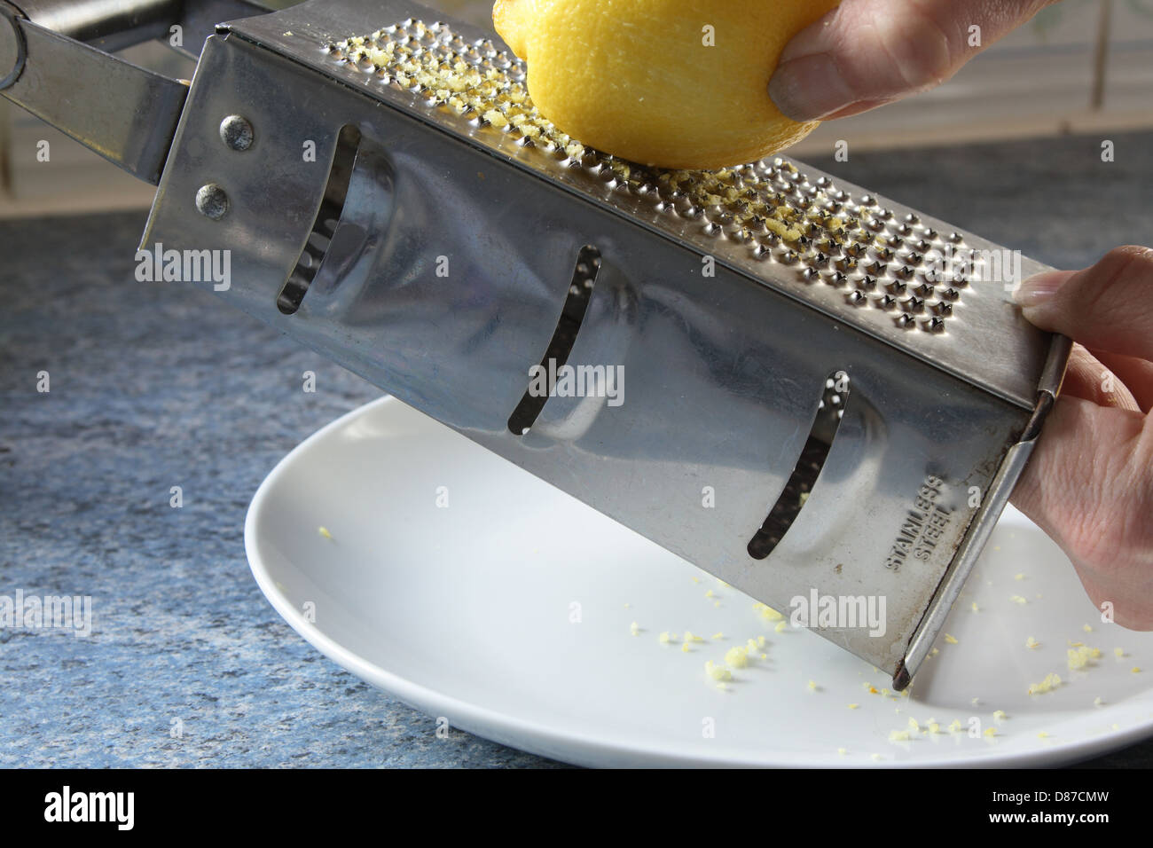 Un limone viene grattugiato, la scorza risultante viene raccolto su una porcellana bianca piastra. Foto Stock