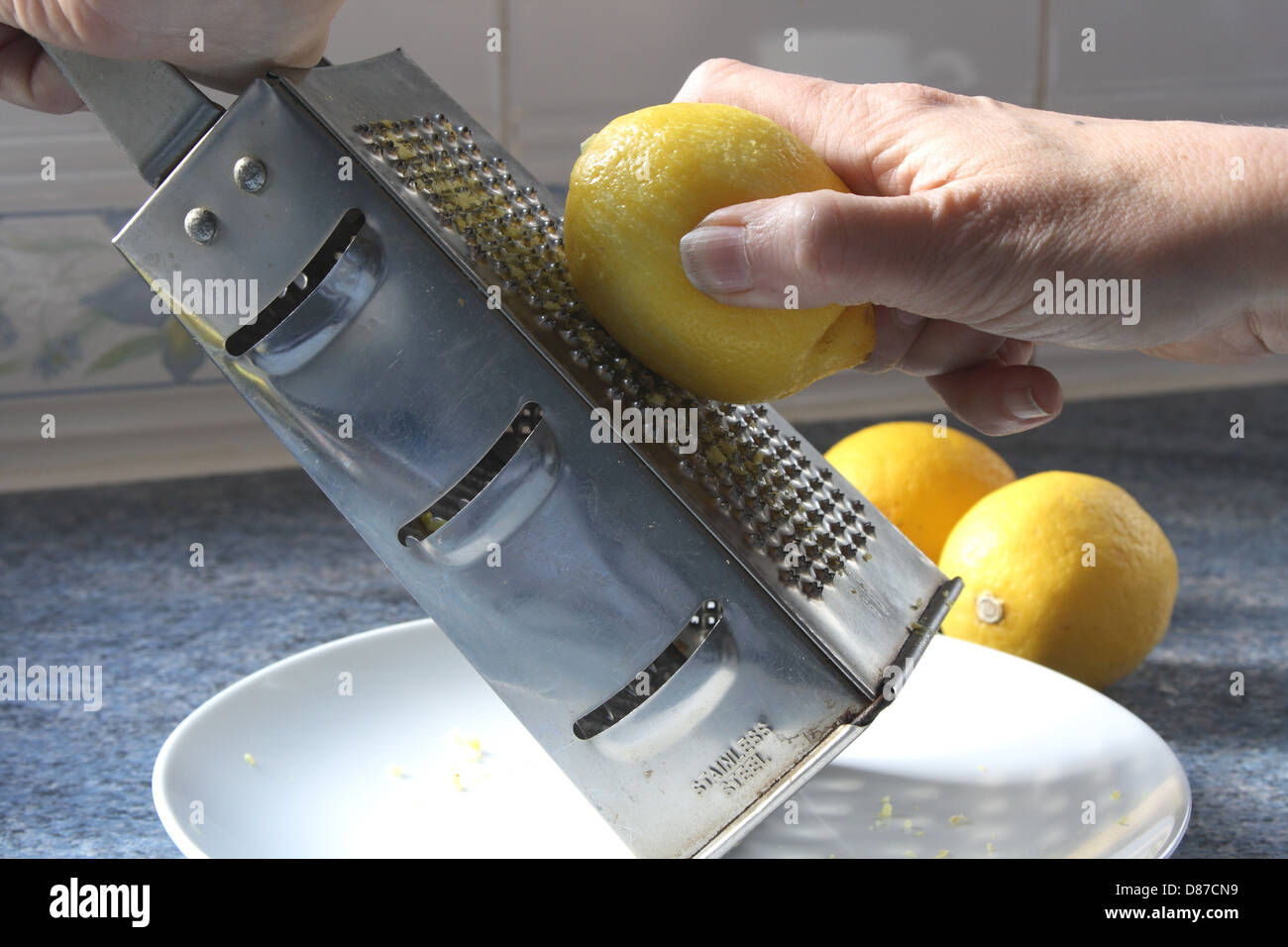Un limone viene grattugiato e la scorza raccolti su di una piastra. Foto Stock