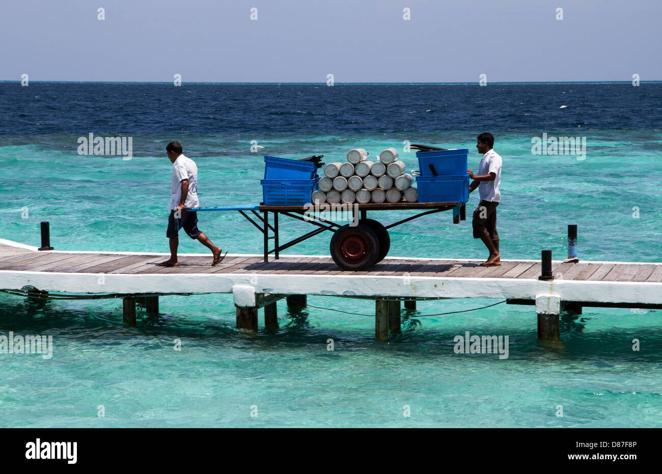 Due uomini il trasporto di bombole per subacquei su un molo nel Maldive nell'Oceano Indiano Foto Stock