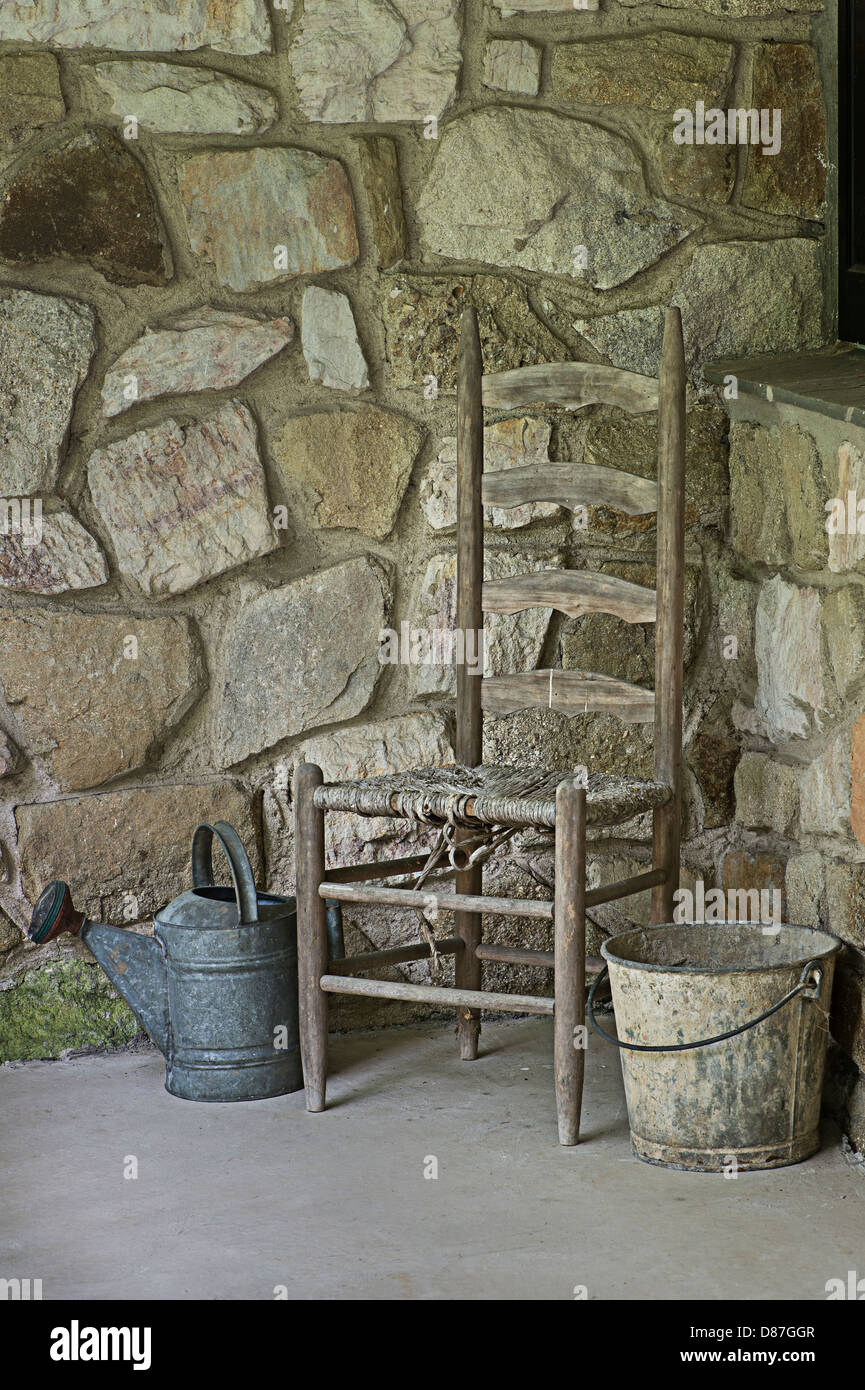 Vecchia sedia, muro di pietra, metallo benna & Annaffiatoio Foto Stock