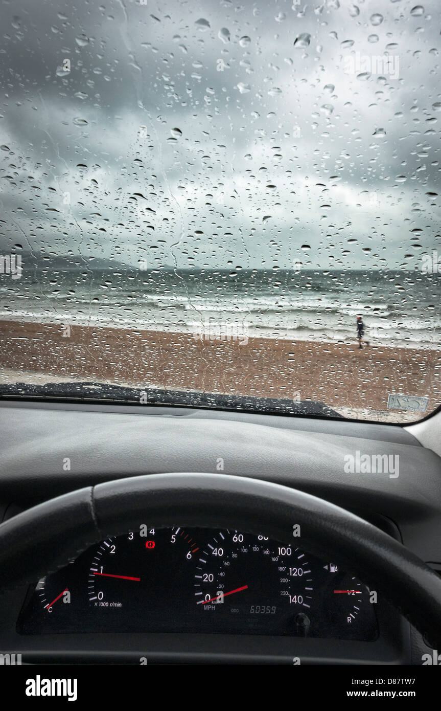 Regno Unito south coast beach attraverso un parabrezza di automobile in un giorno di pioggia in primavera/estate con un uomo che corre Foto Stock